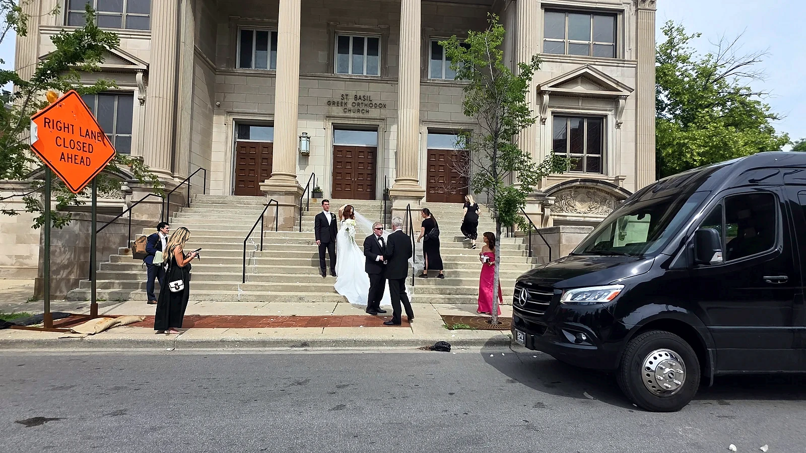 Black Mercedes Sprinter at the steps of a wedding venue with the bridal party